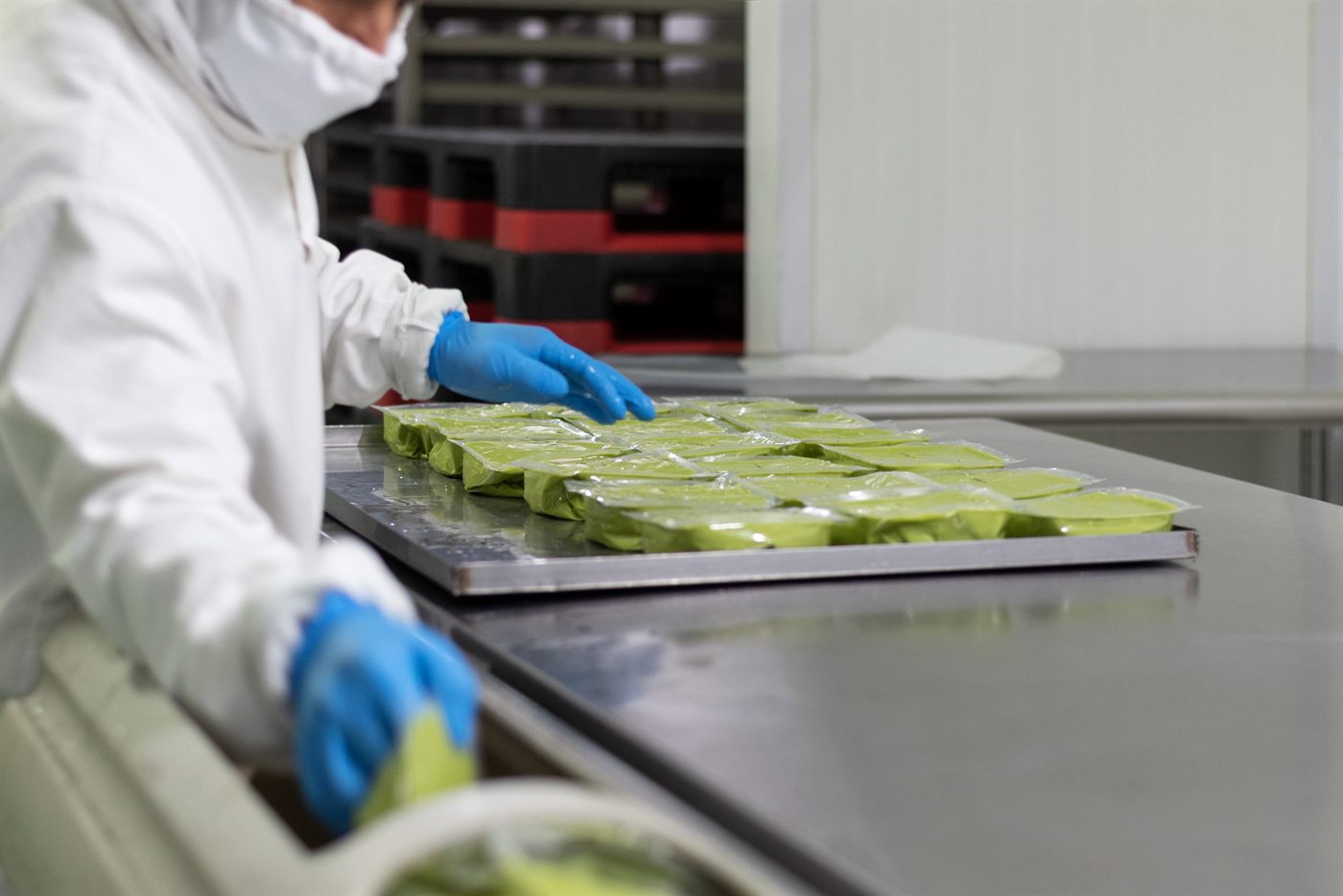 An operator in whites and gloves arranging trays of guacamole on the packing line
